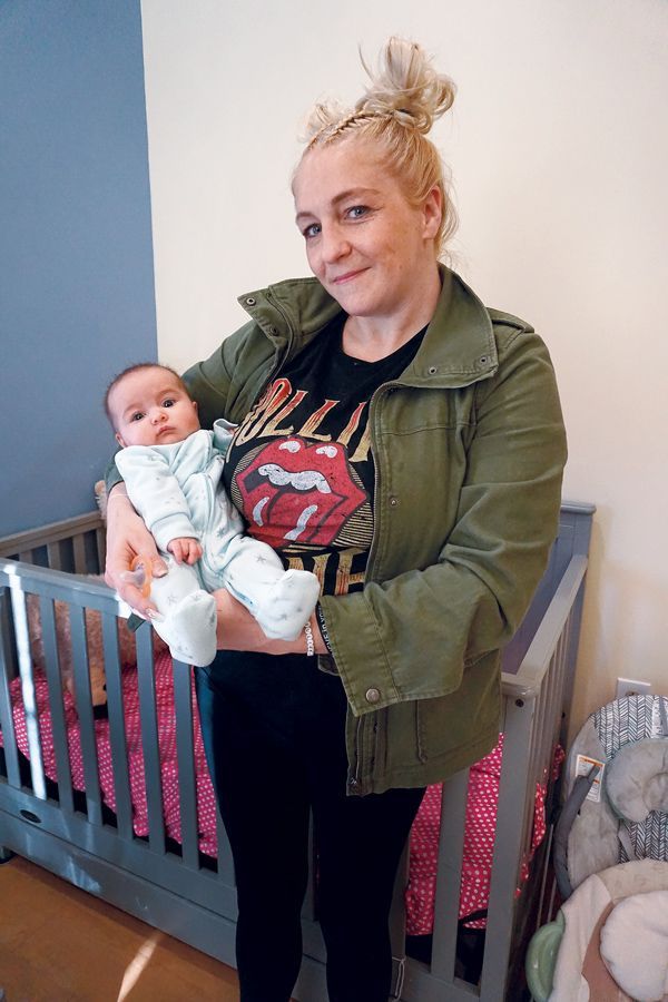 A person holds a baby in their arms in front of a crib in a room with painted blue and cream walls.