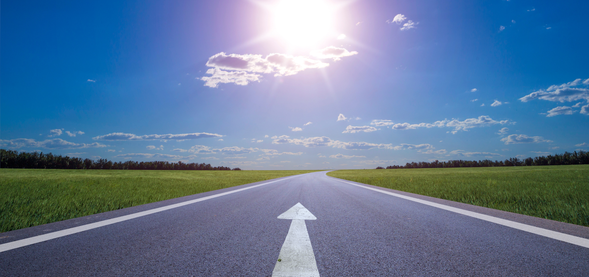 An open road with a forward arrow against a blue sky and sunshine.