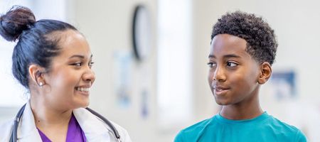 Stock image of a female nurse and a young boy patient smiling at each other.