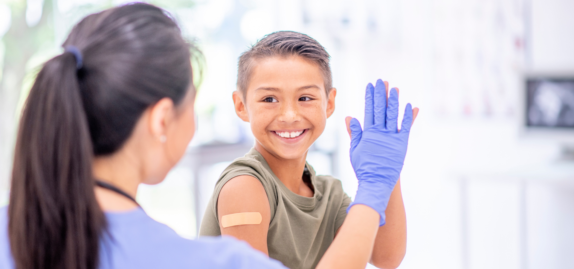 A boy high fives a doctor with a bandaid on his shoulder, presumably after getting a vaccination.