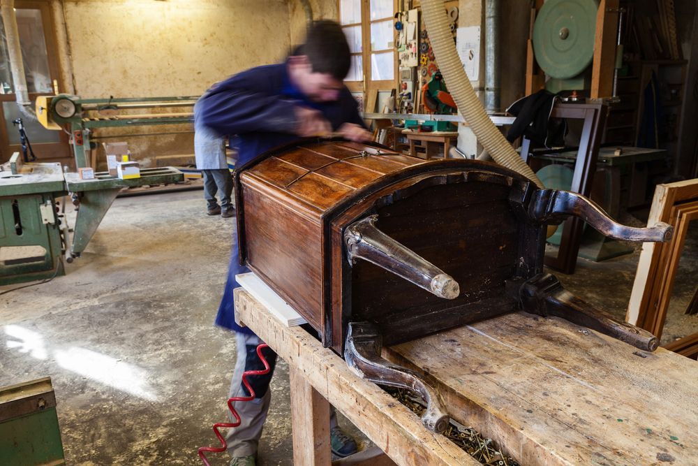 Persona che utilizza un attrezzo per riparare un'antica cassapanca in legno in un laboratorio.