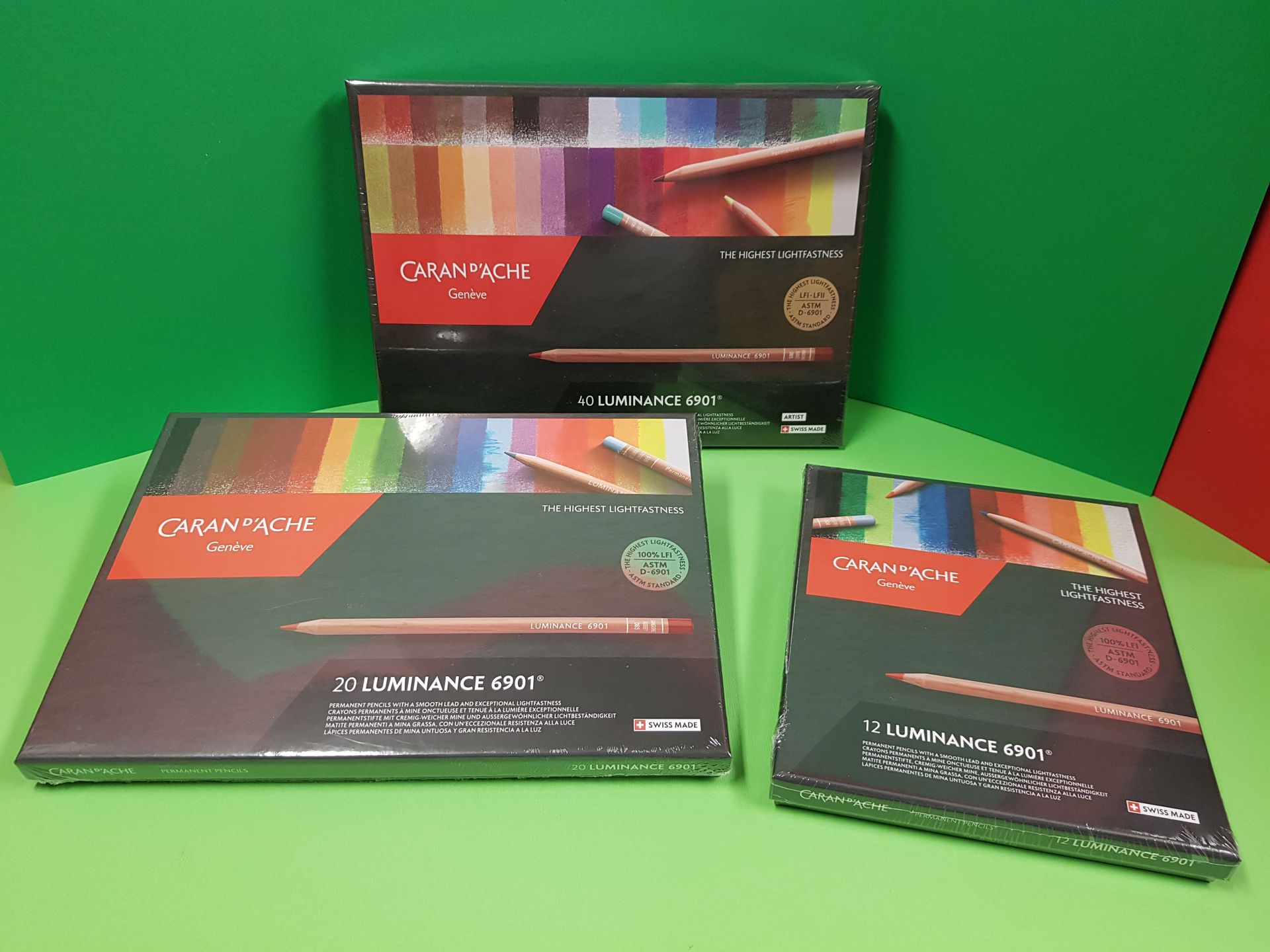 Tre set di matite colorate Caran d'Ache su una superficie verde con sfondo verde e rosso.