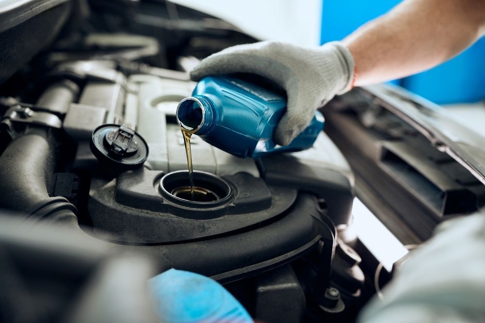 A Person Is Pouring Oil Into A Car Engine — Tuned Suspension & Mechanic in Parkes, NSW