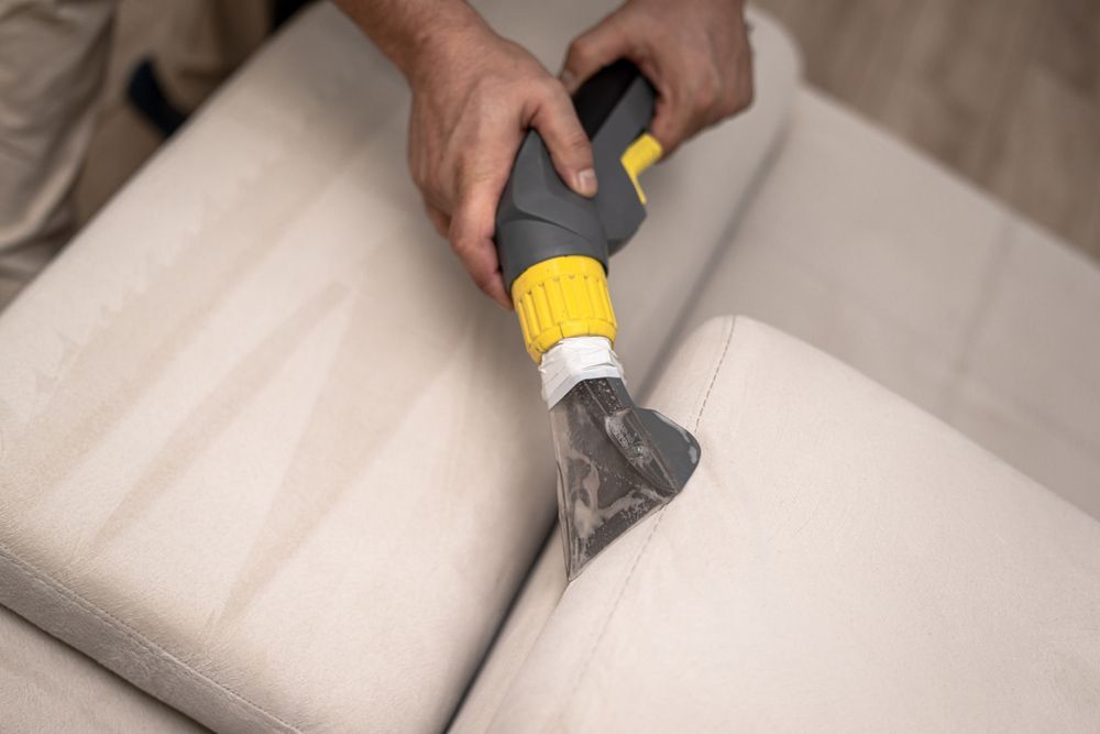 A Person Is Cleaning A Couch With A Vacuum Cleaner — Allwood Upholstery In Manunda, QLD