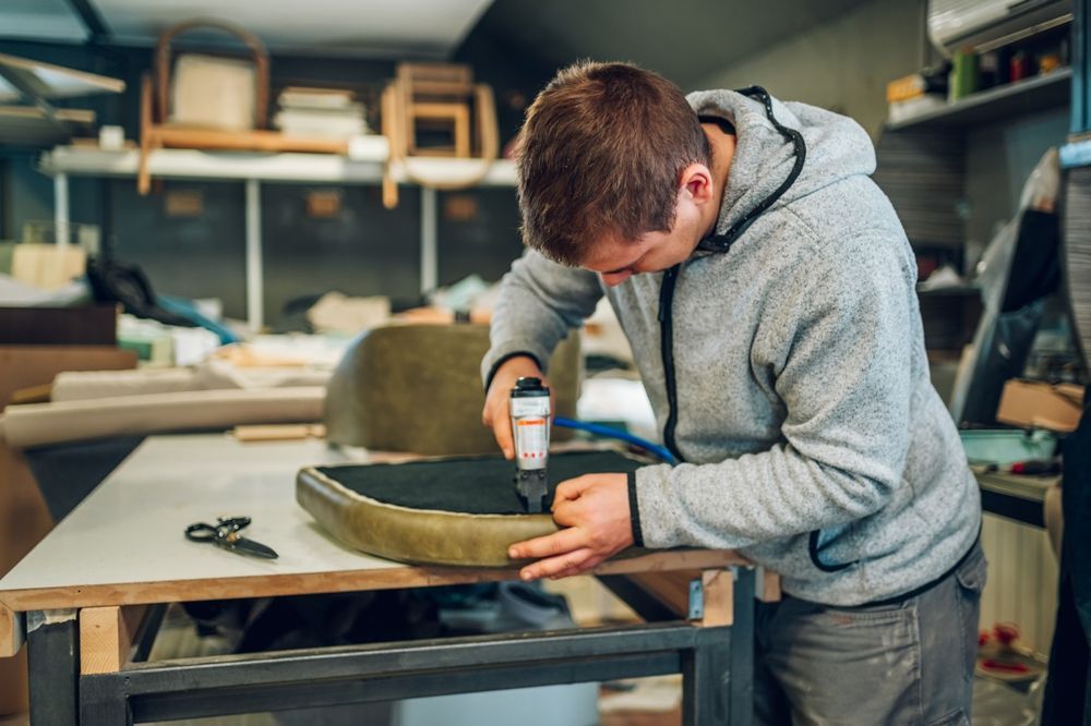 A Man Is Working On A Chair In A Workshop — Allwood Upholstery In Manunda, QLD