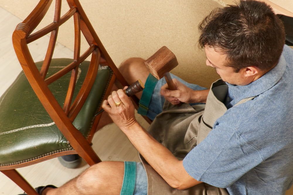A Man Is Working On A Chair With A Hammer — Allwood Upholstery In Manunda, QLD