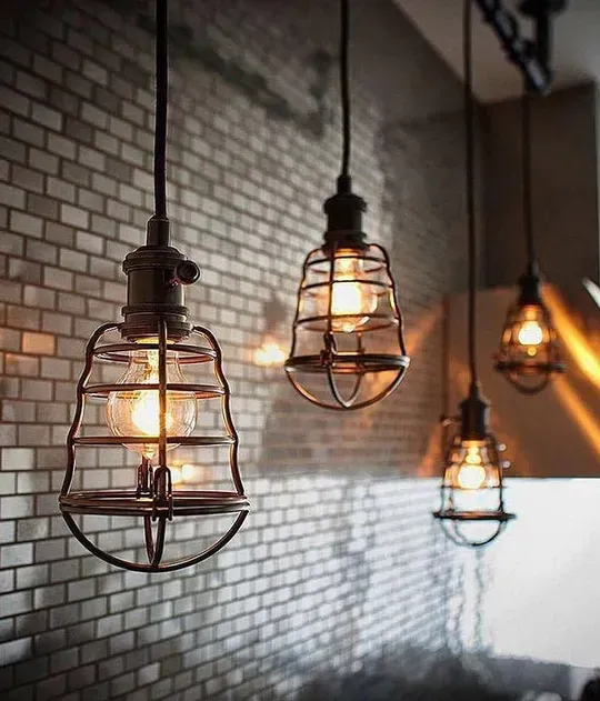 A row of pendant lights hanging from the ceiling in front of a brick wall.