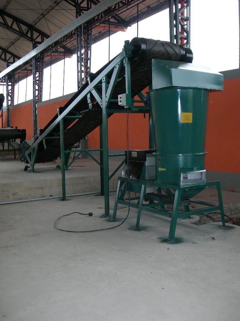Máquina industrial con tolva verde y cinta transportadora en un almacén de fábrica.