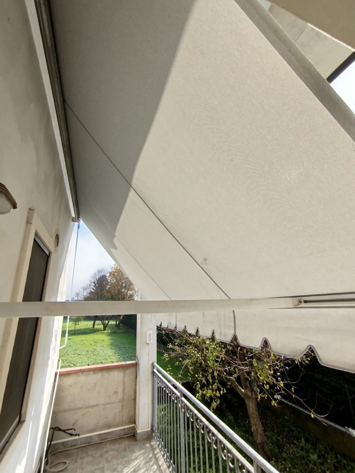 Un balcone con una tenda bianca sopra e vista sul giardino.