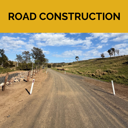 A dirt road with trees on the side and a blue sky, you can see the repaired hillside that was once eroded into a riverbed.