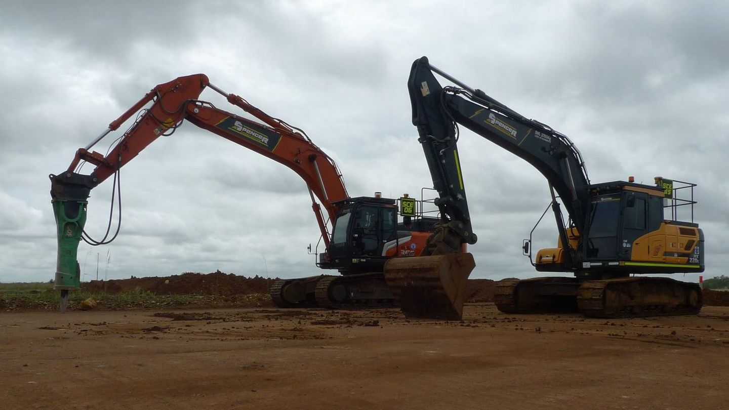 Two Spencer Civil & Earthworks excavators are parked next to each other on a dirt pad.
