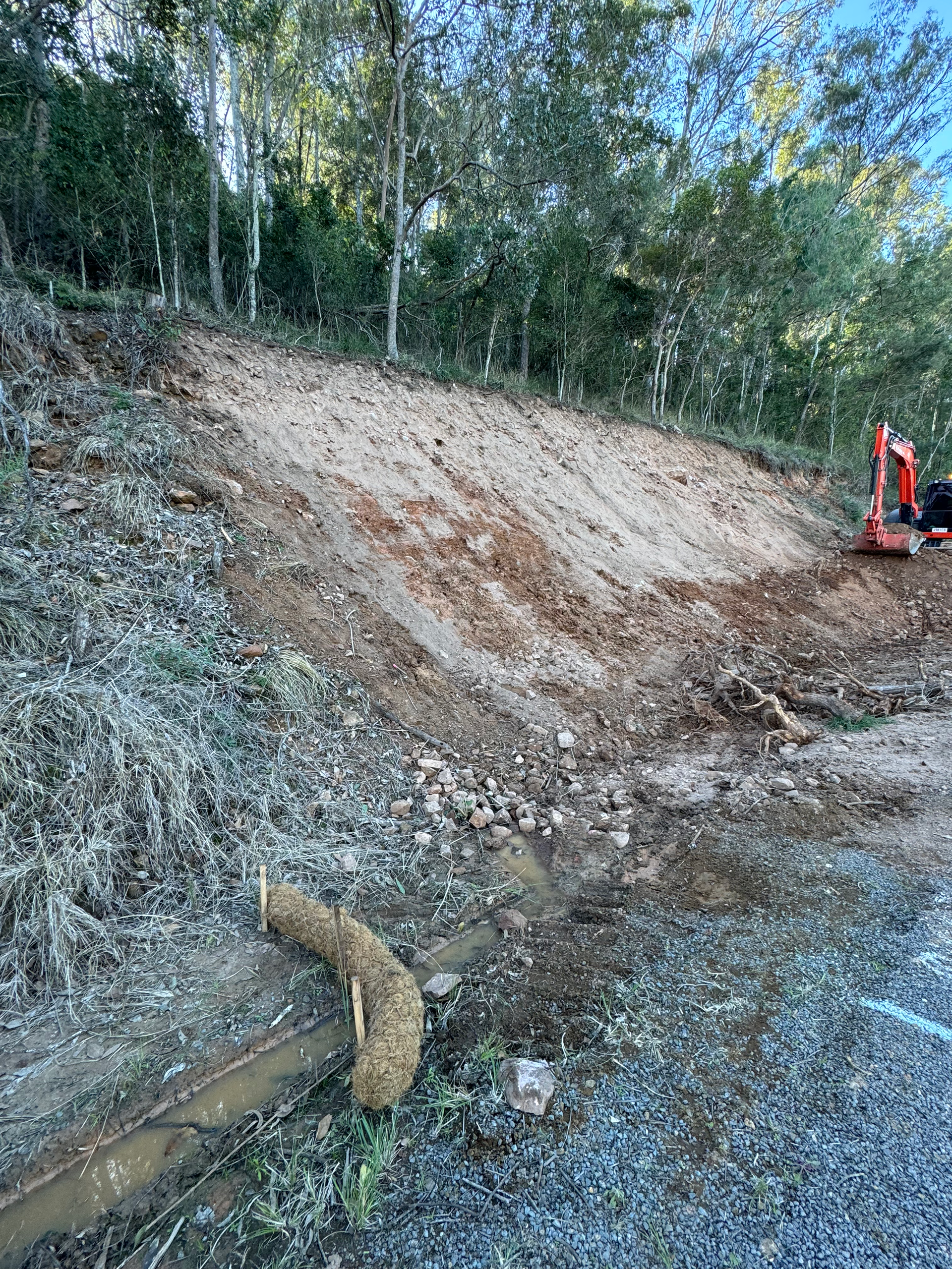An excavator is working on clearing away debris after a slip occurred on a hill next to a roadway.