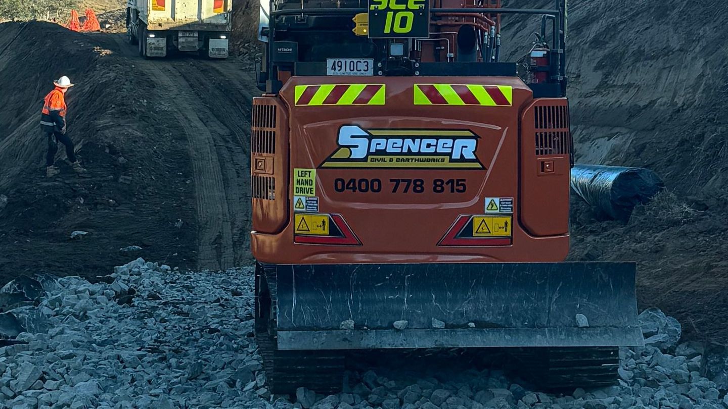 A spencer civil & earthworks excavator is spreading rocks along a path.