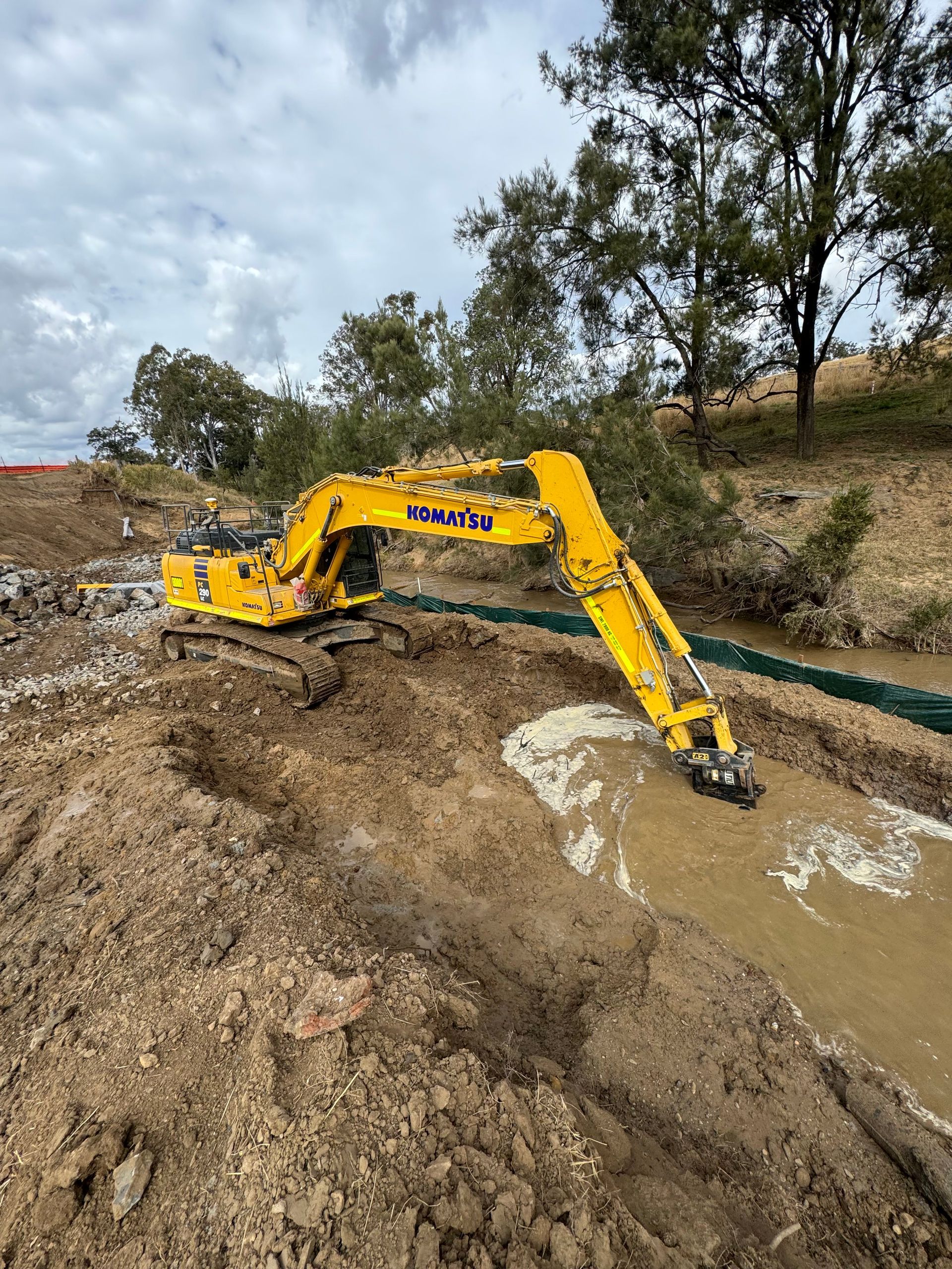 A yellow Spencer Civil & Earthworks excavator is clearing dirt from a waterway.
