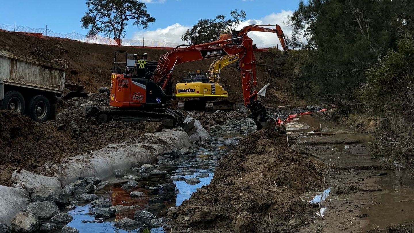 A couple of spencer civil & earthworks excavators are working on a muddy river.