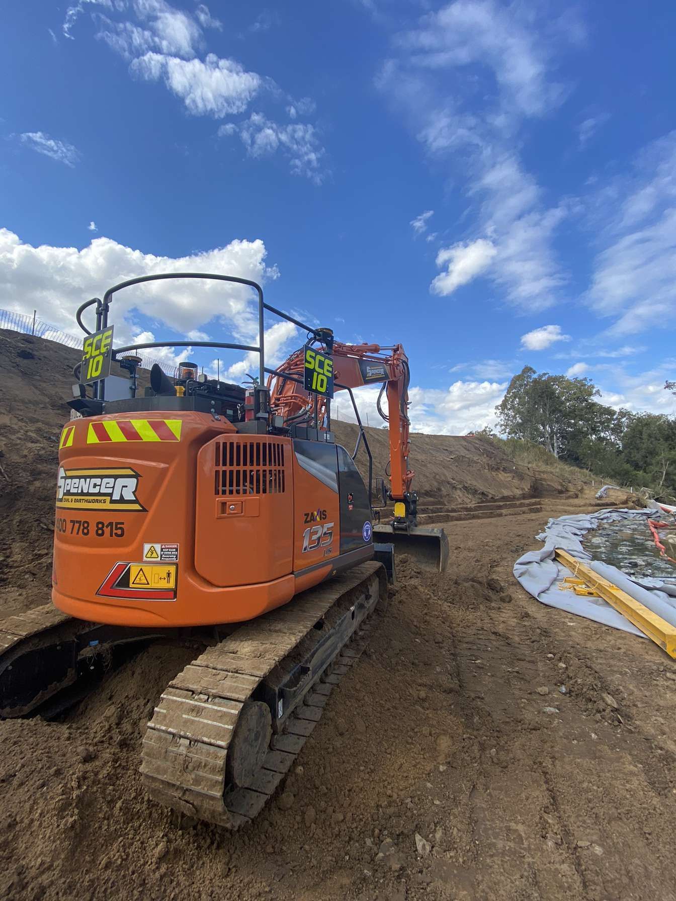 A spencer civil & earthworks excavator is levelling the surface of a riverbed.