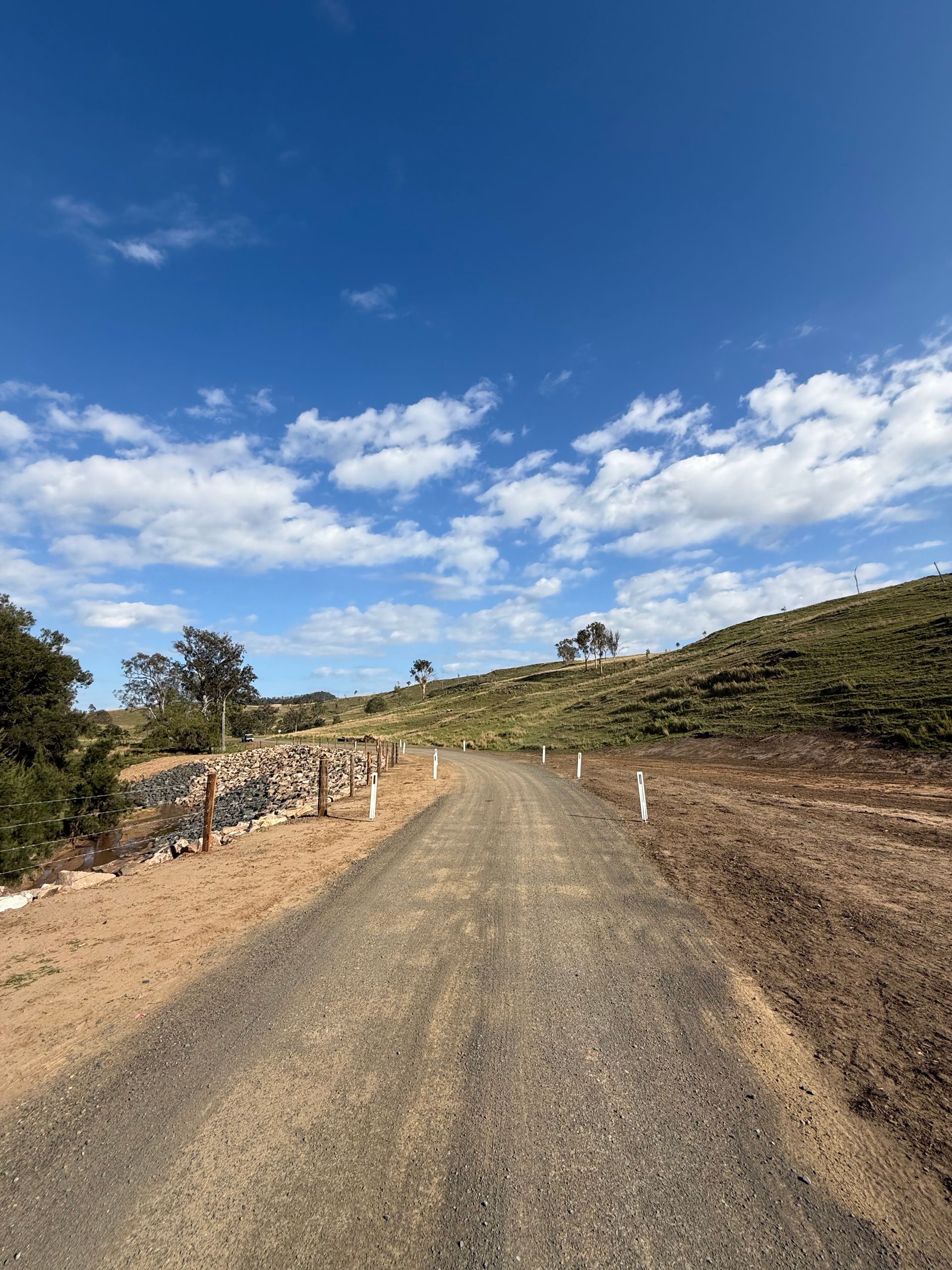 A dirt road with a repaired river bank sloping down to the left side.