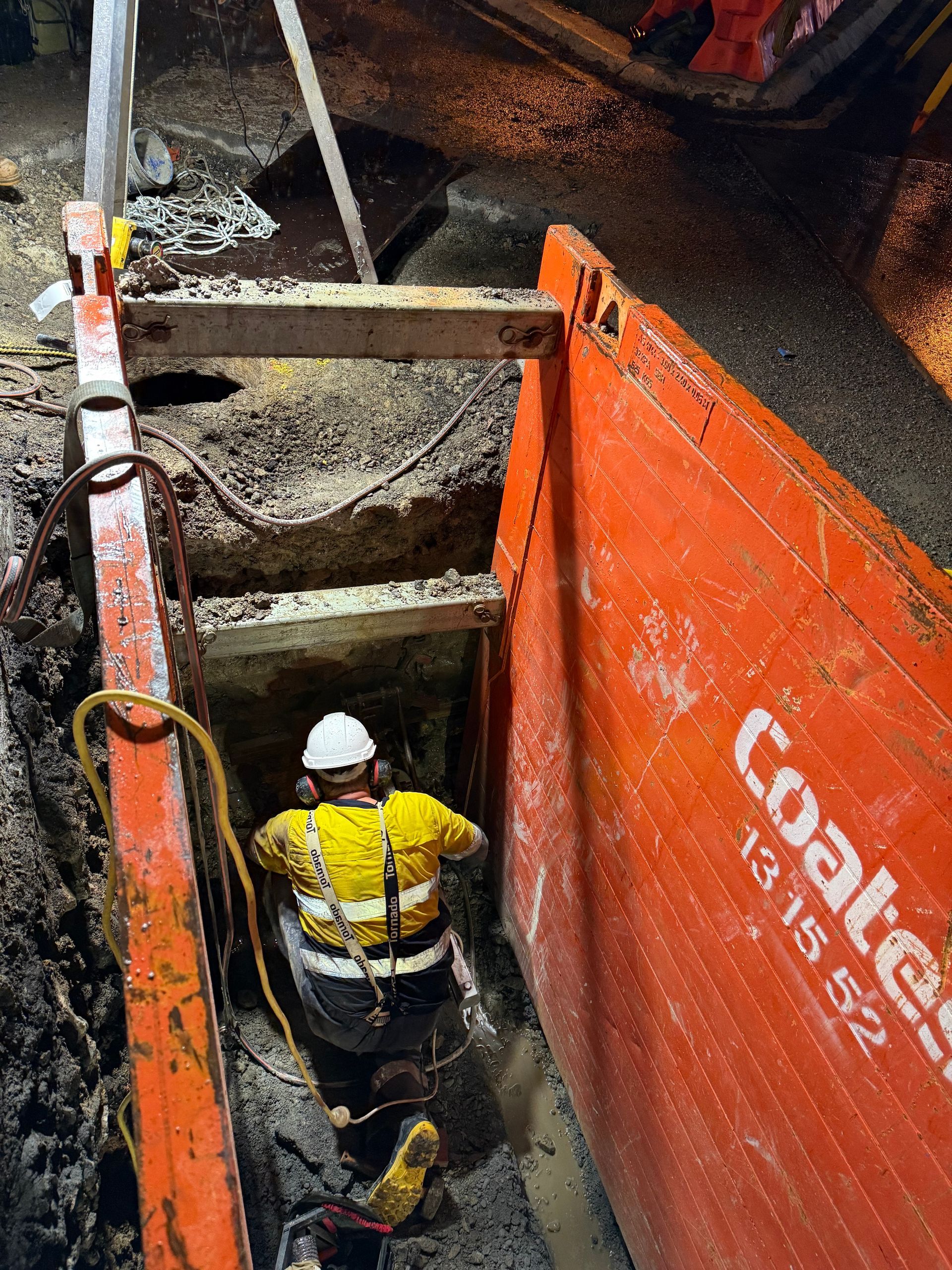 A man in a reinforced hole in the street excavating around underground assets with power tools.