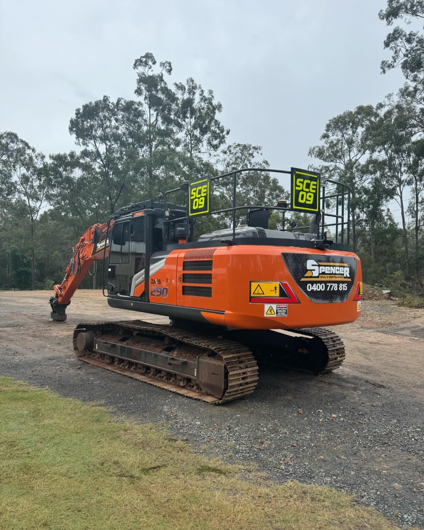 A large orange Spencer civil & earthworks excavator is parked on a dirt pad.