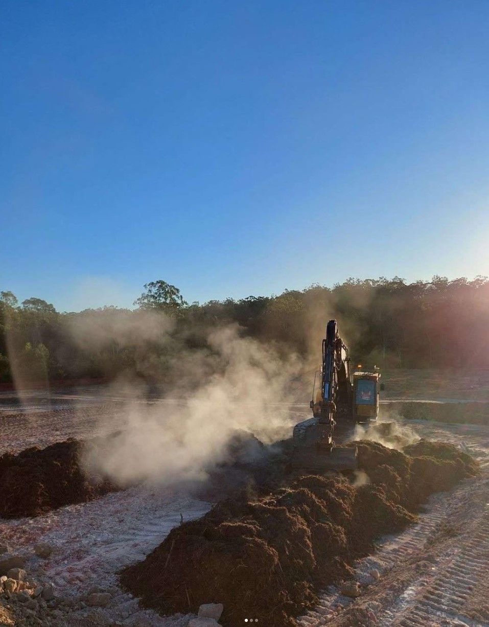 A Spencer Civil & Earthworks excavator is moving dirt on a cold morning in a field with steam coming out of it.