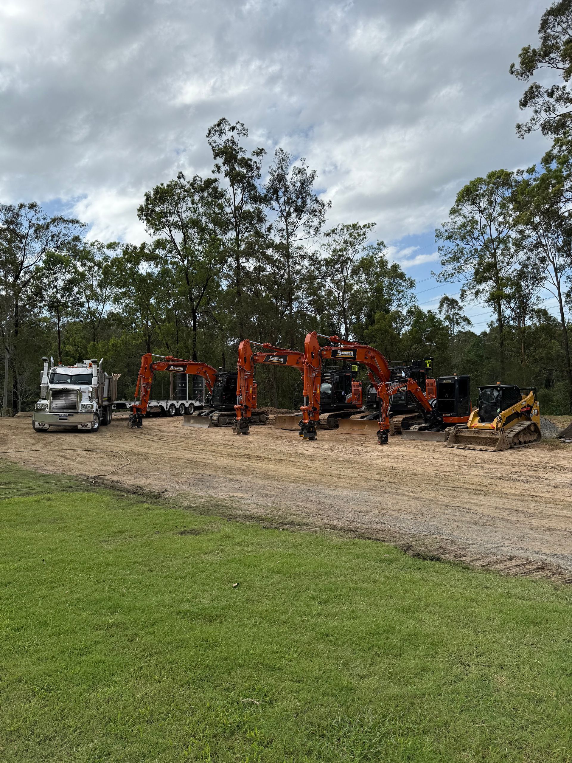 A truck is parked on a dirt pad next to a row of Spencer Civil & Earthworks equipment.