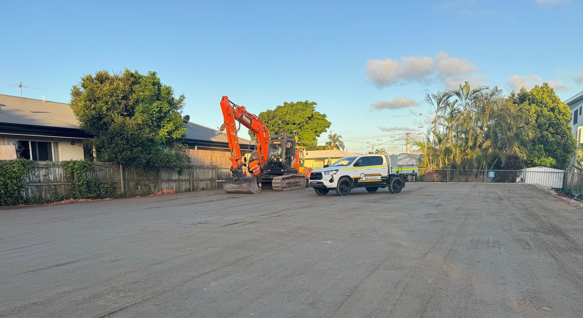 A white Spencer civil & earthworks ute is parked in a dirt lot next to one of their excavators.