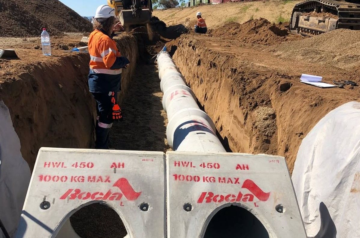 A man is standing in a trench next to a large stormwater pipe.