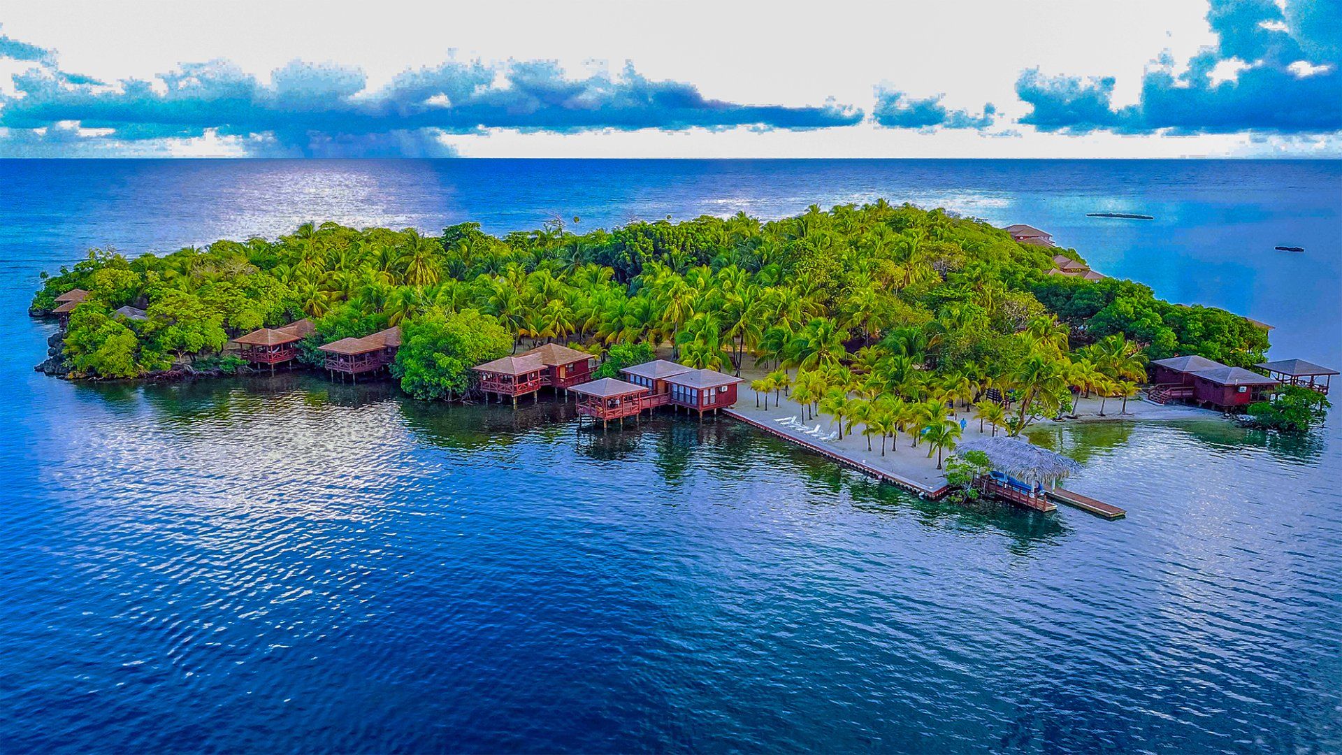 Island with lush green trees and wooden buildings over turquoise water.
