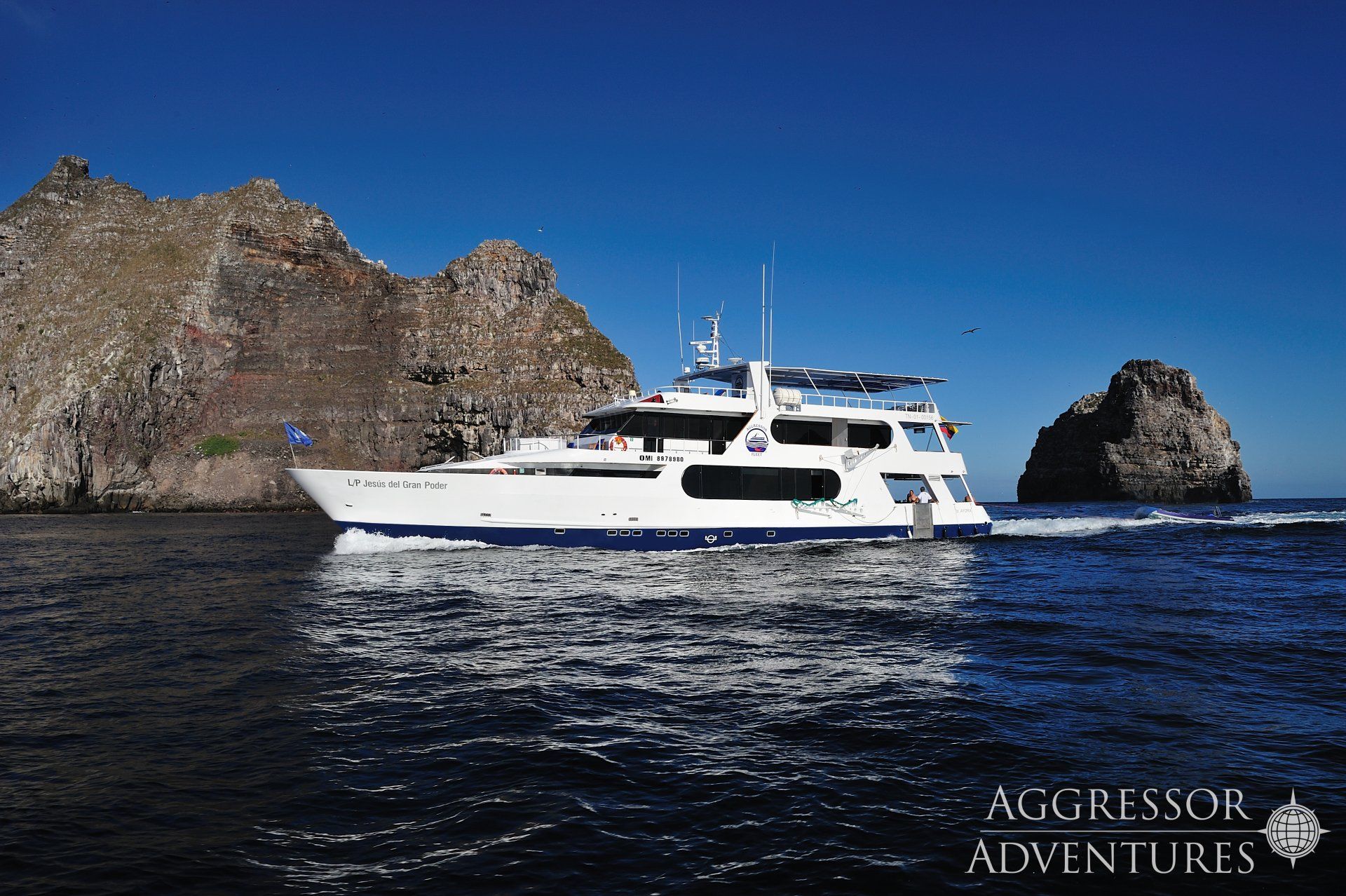 White boat with blue accents near rocky islands on a sunny day.