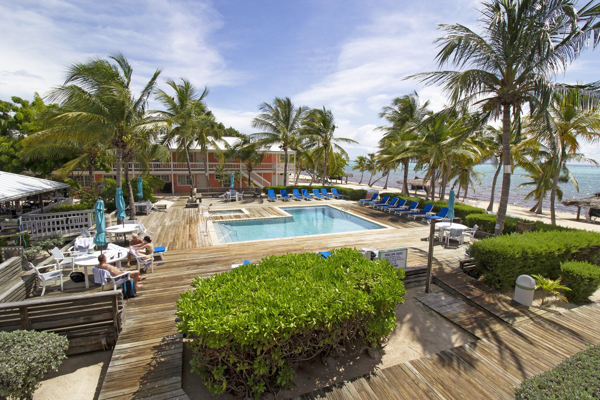Tropical resort with pool, beach, palm trees, and people.