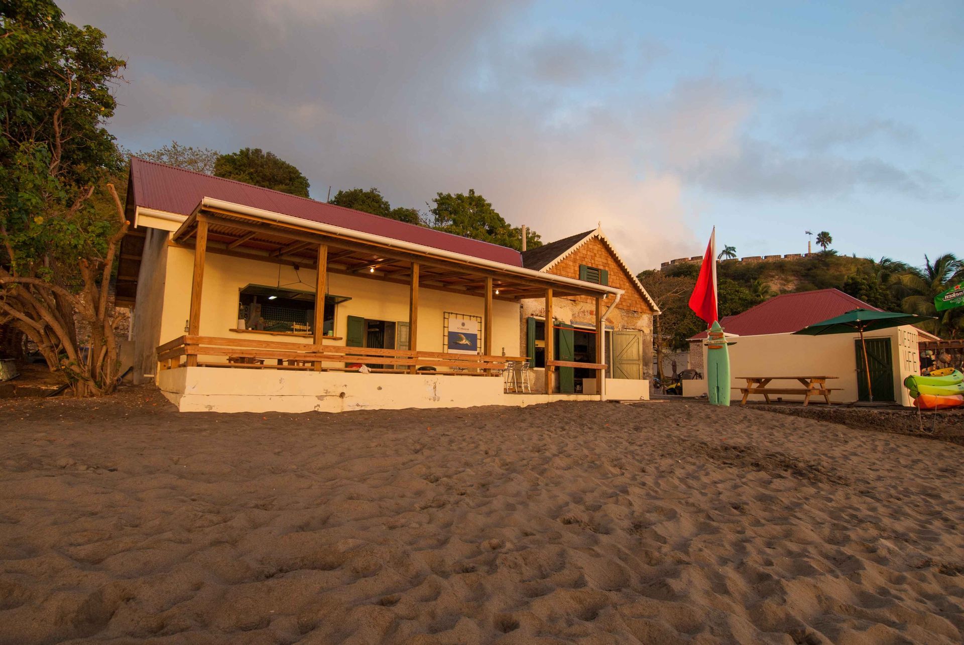 Beachside buildings with wooden decks and red roofs on a sandy beach.