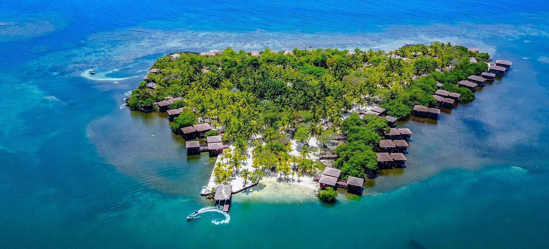 Aerial view of a tropical island with overwater bungalows and lush greenery surrounded by turquoise water.