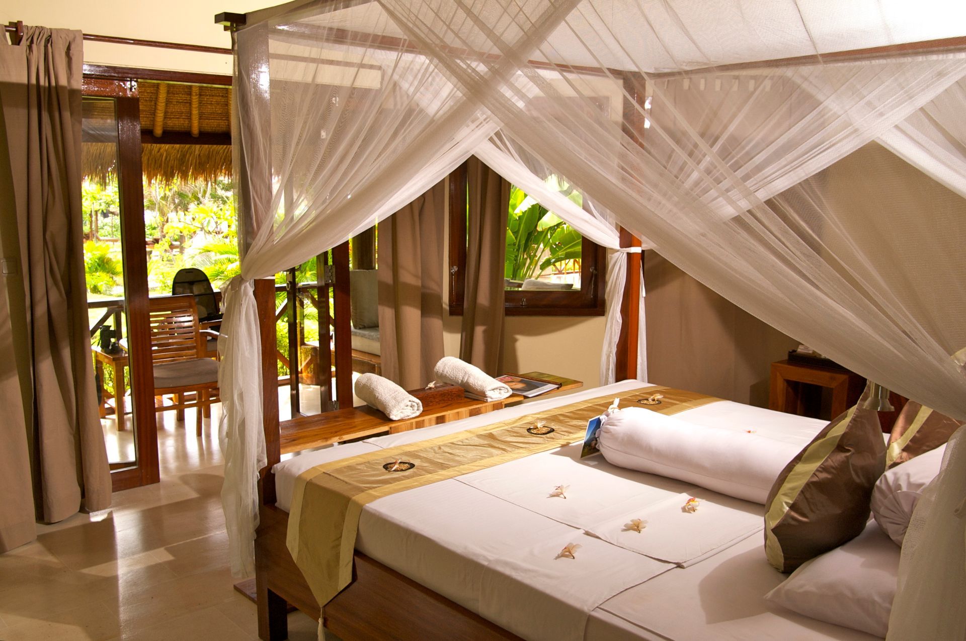 Bedroom with canopy bed, towels, and a balcony overlooking greenery.