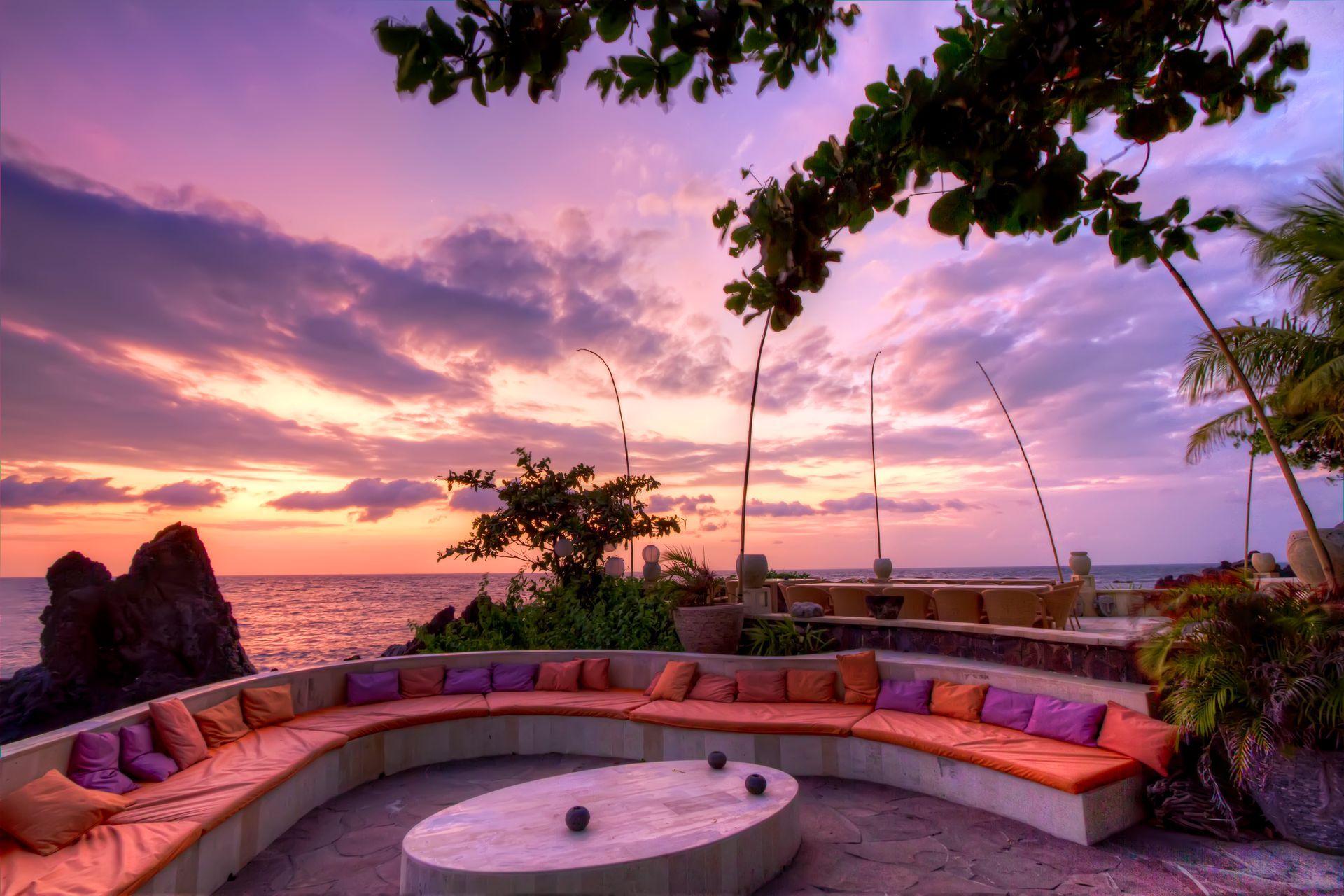 Sunset view with curved seating area overlooking the ocean, orange and purple hues.