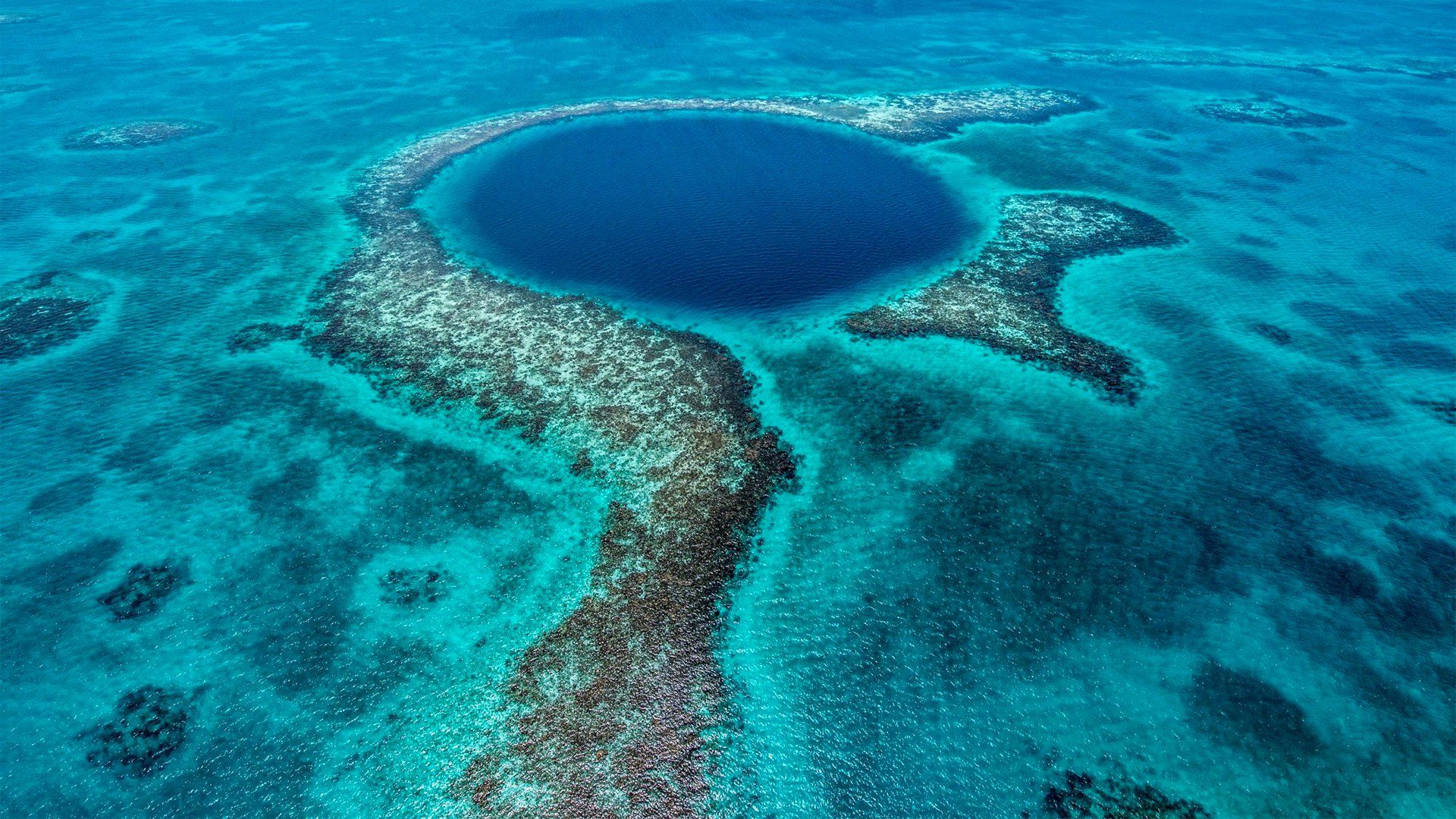 Blue Hole in Belize, a large underwater sinkhole surrounded by coral reefs, viewed from above.