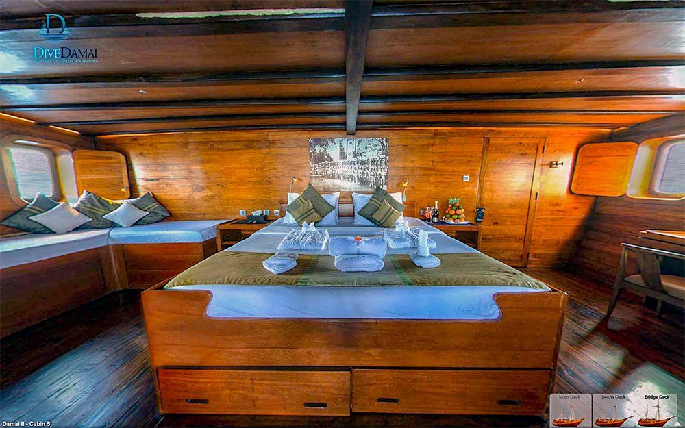 Wooden cabin interior on a boat, featuring a large bed, seating, and windows.