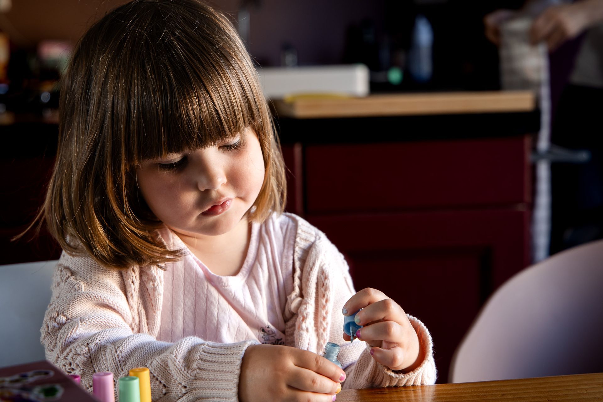 Kind speelt geconcentreerd met nagellak aan tafel tijdens rustig moment thuis