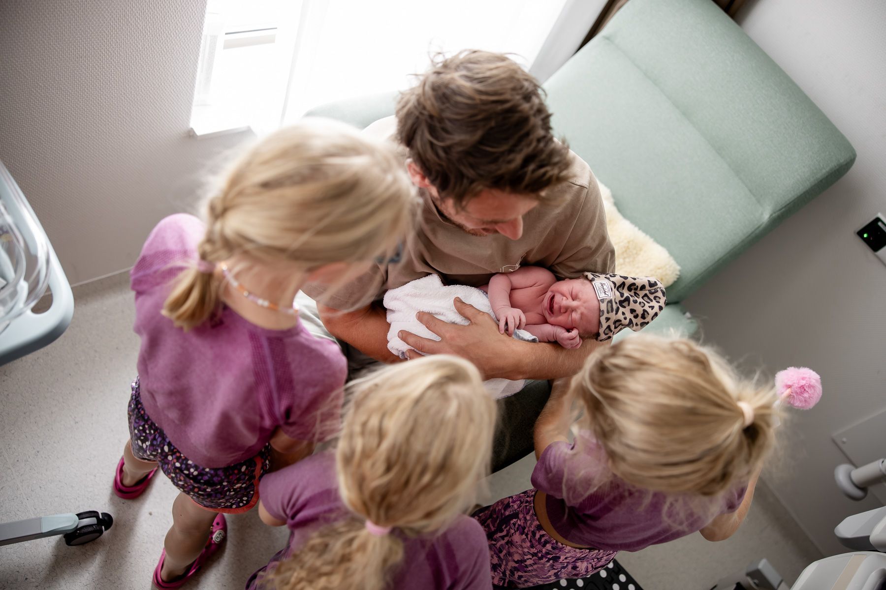 Vader houdt pasgeboren baby vast terwijl broertjes en zusjes komen kijken