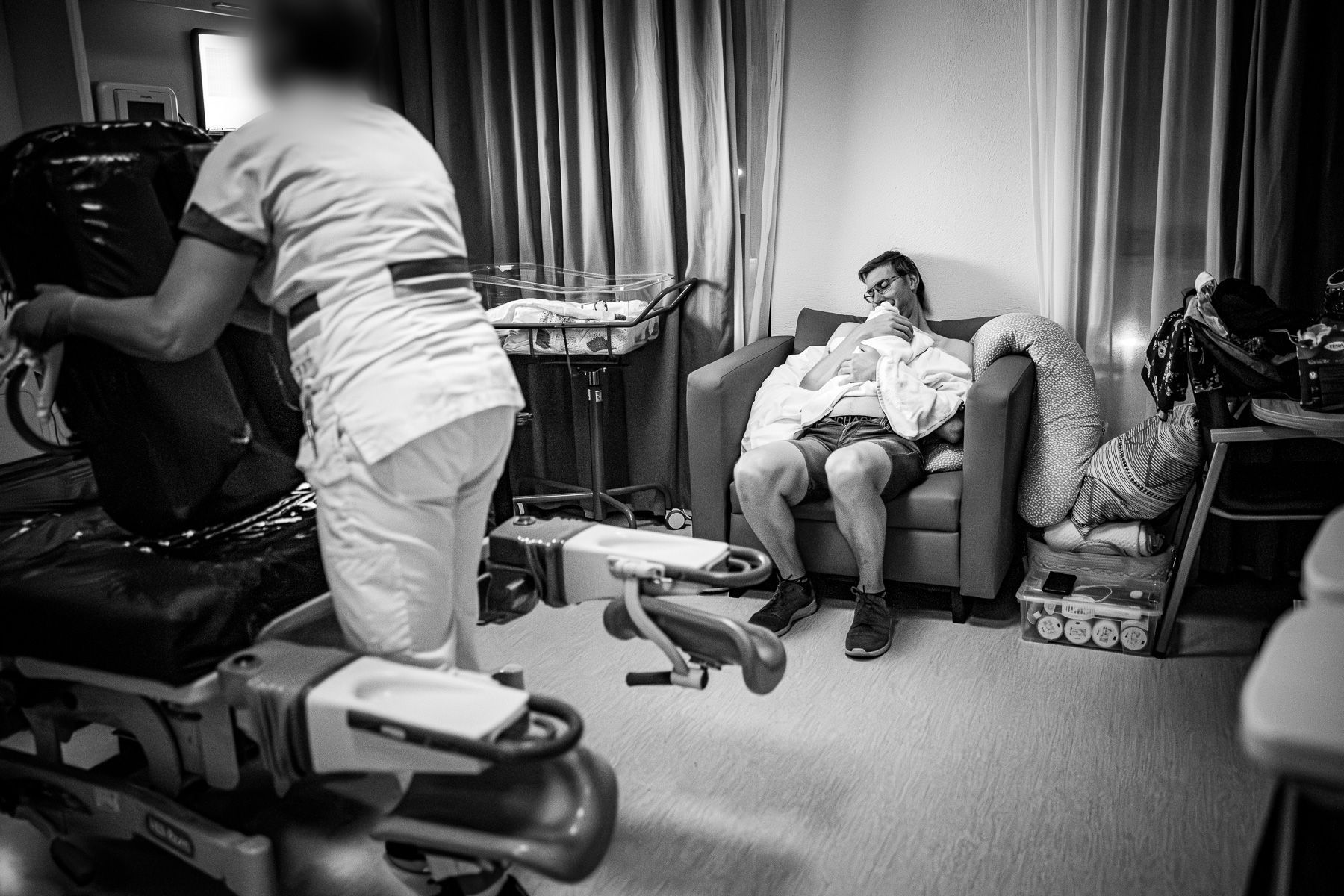 Vader zit met zijn pasgeboren baby in de ziekenhuiskamer terwijl kamer wordt schoongemaakt door ziekenhuispersoneel