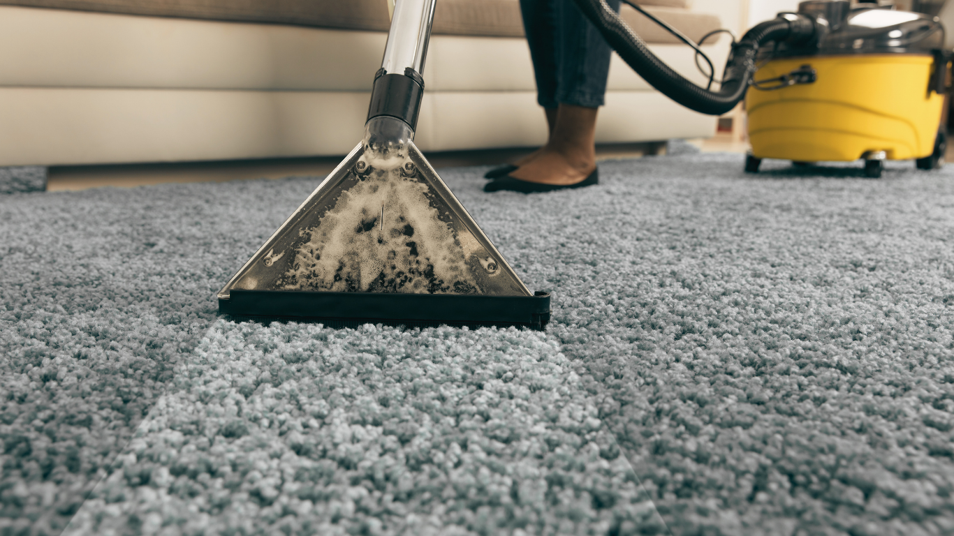 Person vacuuming a blue carpet with a yellow wet/dry vacuum cleaner.