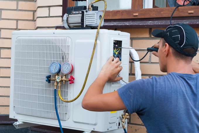 Technician checking an outdoor air conditioner unit with gauges attached.