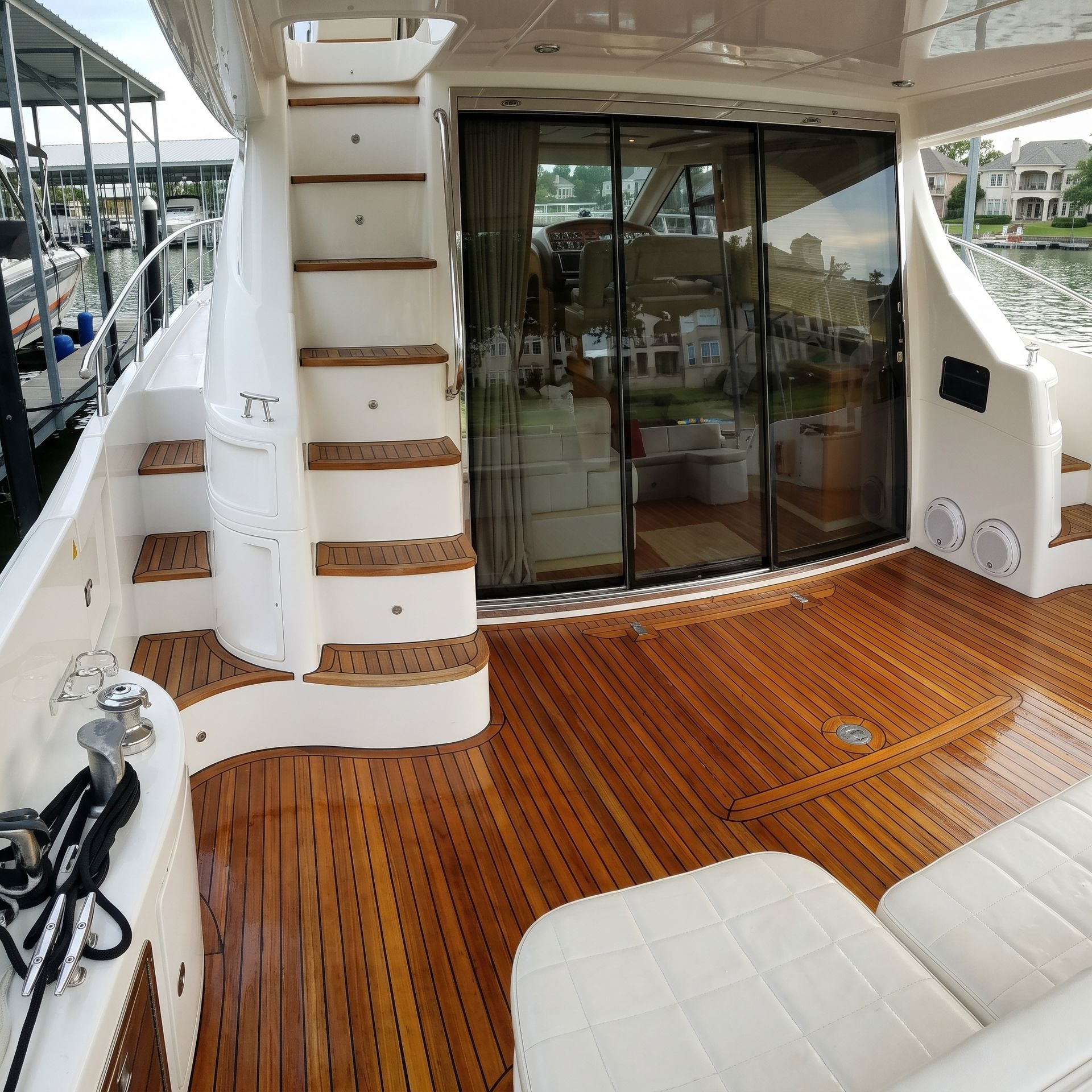 Yacht stern deck with teak flooring, sliding glass doors, and white stairs beside marina boats