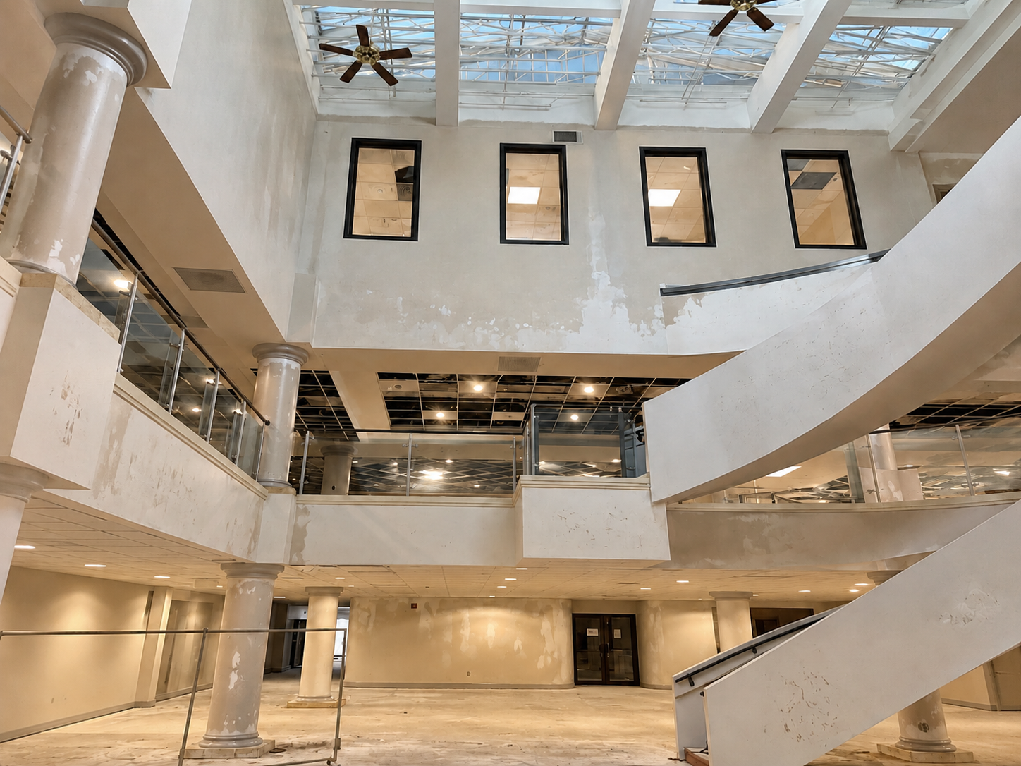 Abandoned multi-level atrium interior with damaged stairs, open skylights, and broken windows