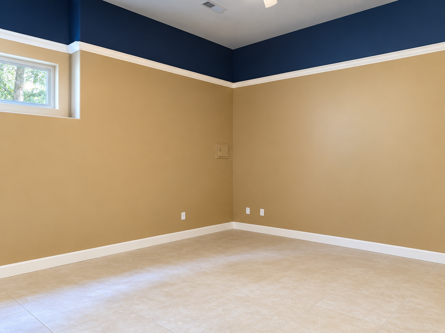 Empty beige room with white trim, dark blue ceiling border, and a small window.