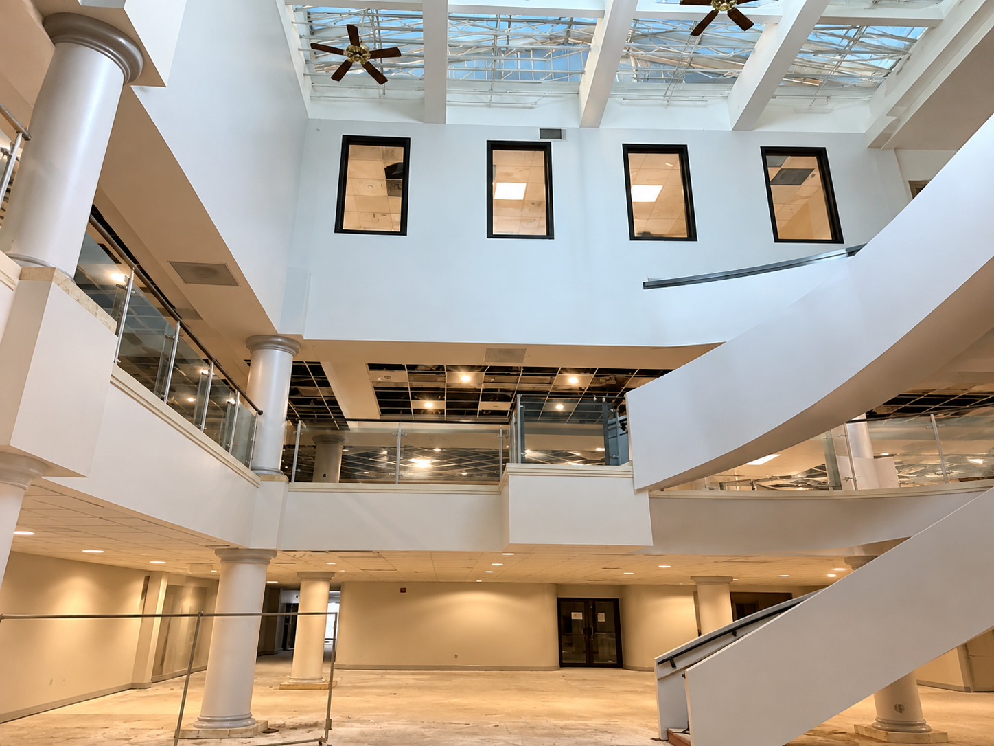 Modern atrium with curved white stairs, skylit ceiling, and tall windows in a bright interior hall