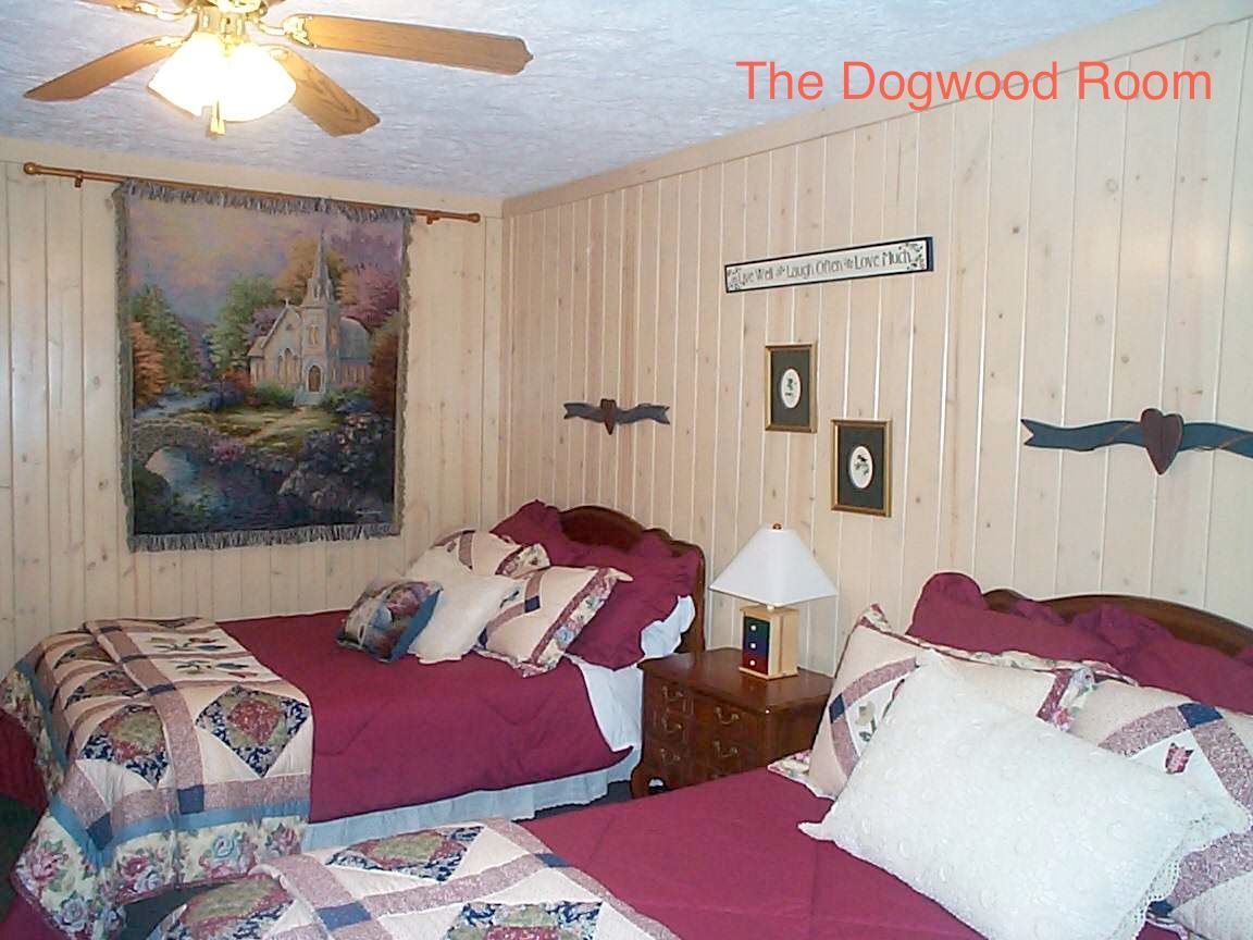 Dogwood Room with two beds, floral quilts, burgundy linens, wood-paneled walls, and tapestry artwork.
