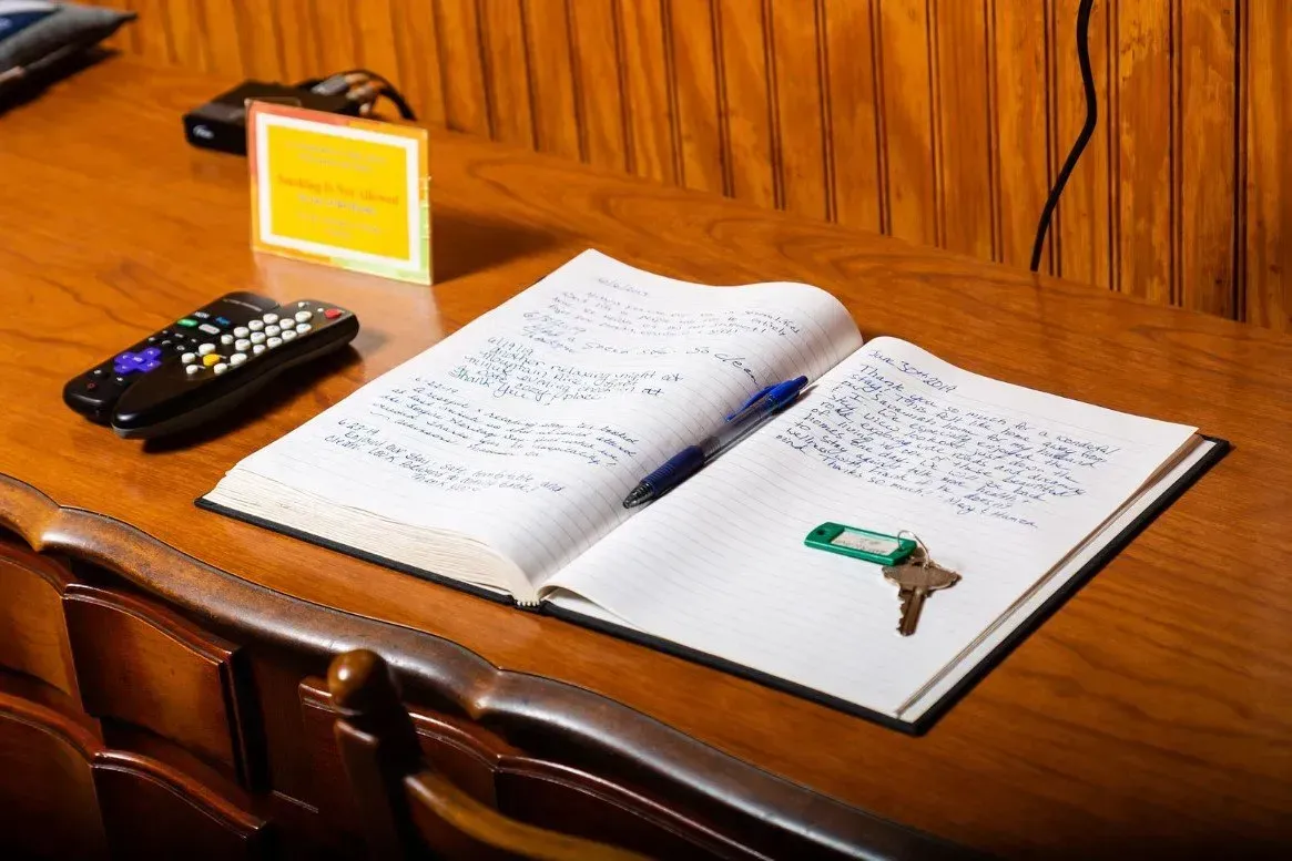 Open notebook with pen and key, next to a remote and sign on a wooden desk.