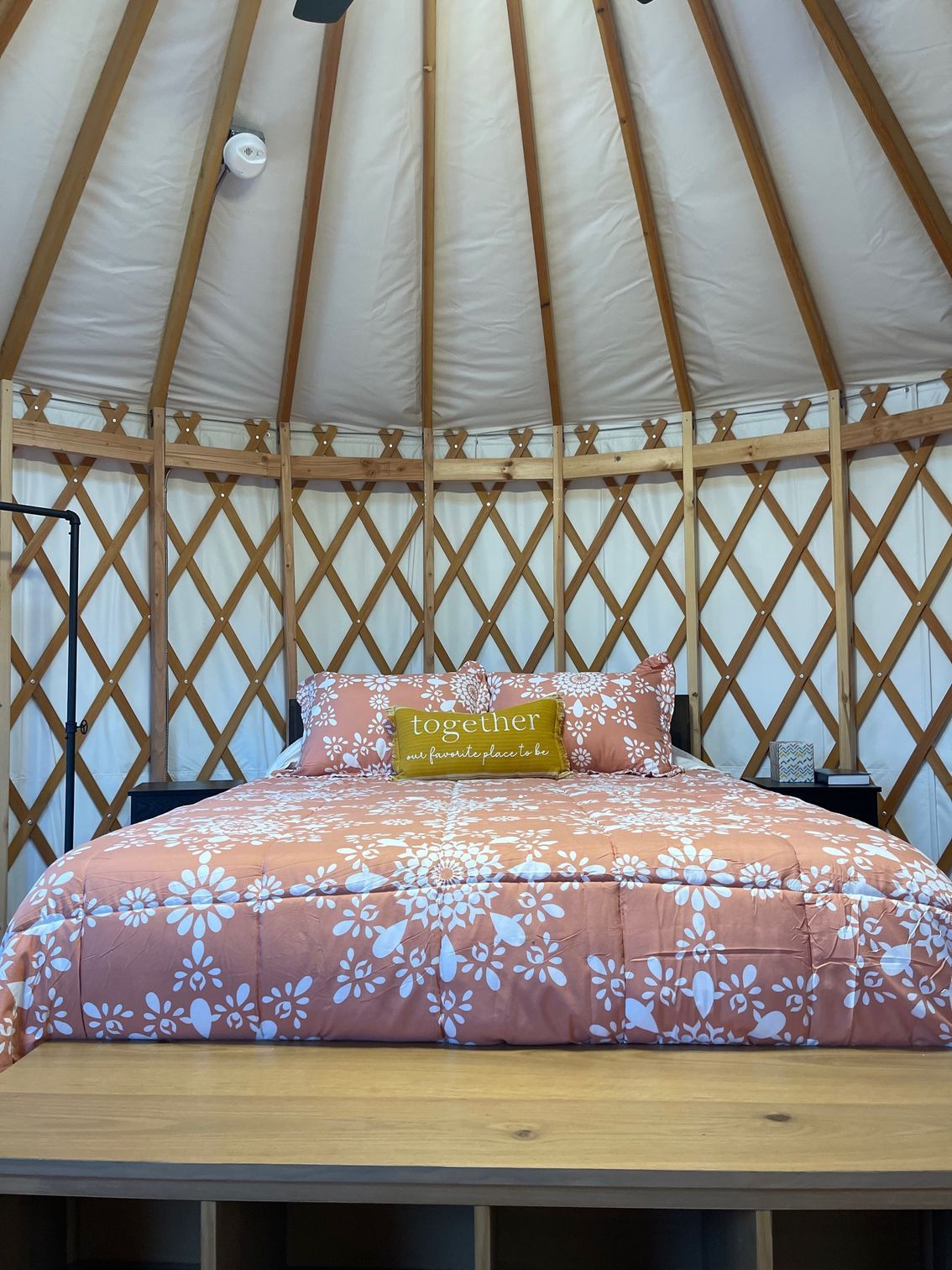A cozy yurt interior with a bed covered in peach floral bedding, topped with a gold pillow.