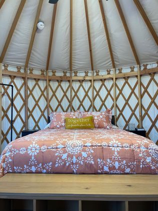 Bed with floral bedding inside a yurt with wooden lattice walls and white ceiling.