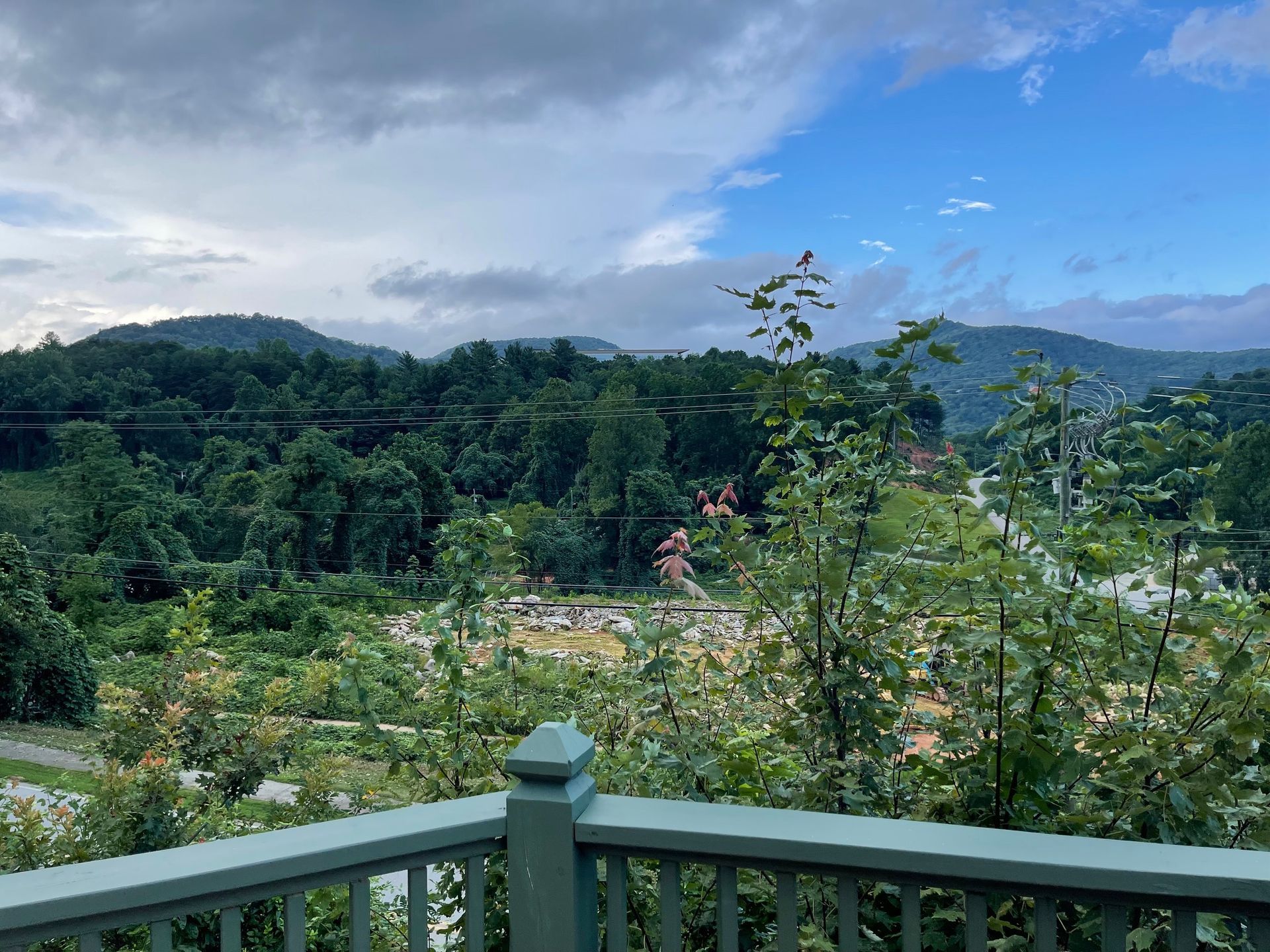 View from a deck overlooking lush green mountains under a partly cloudy sky.